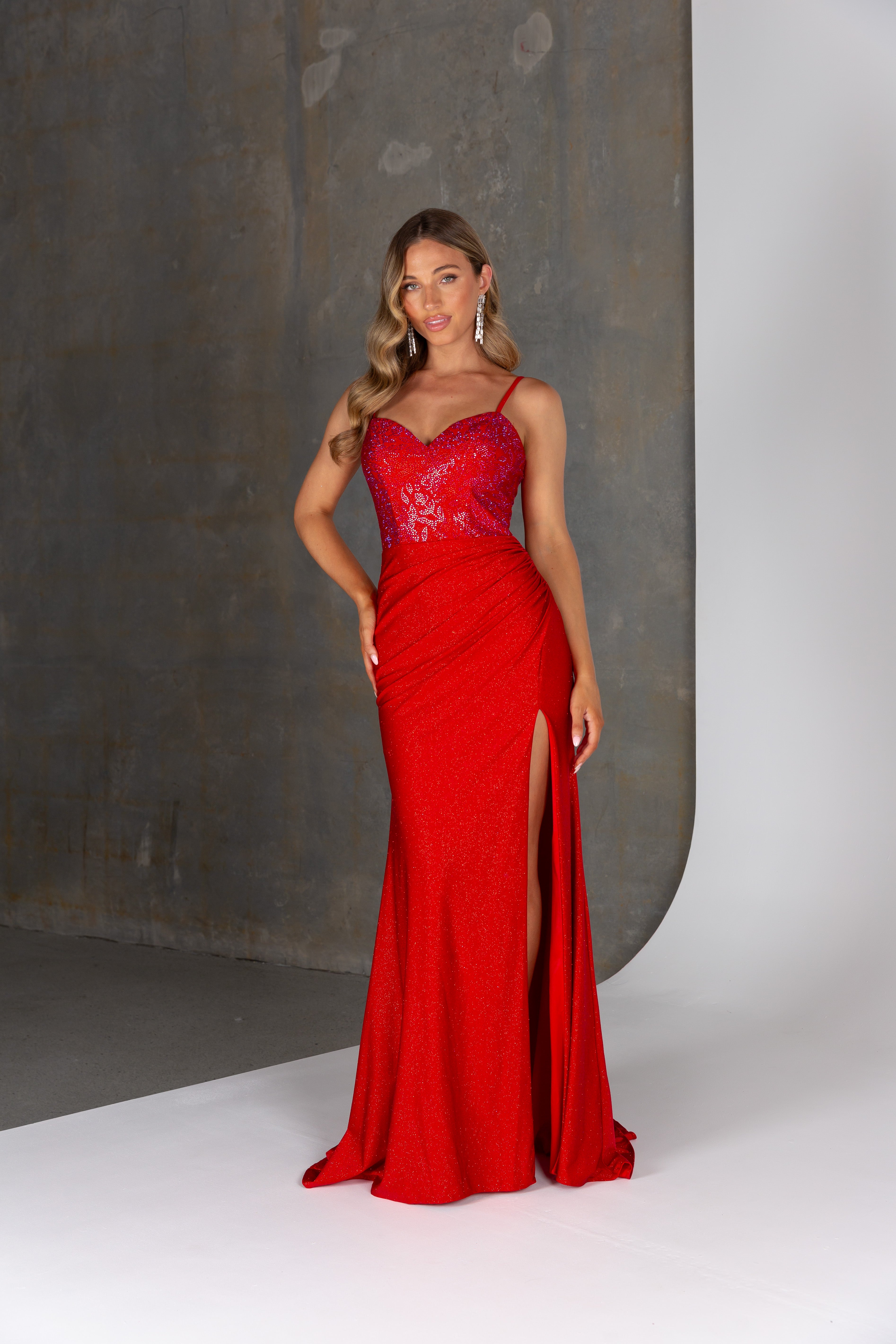 Woman wearing a red evening gown with a high slit against a neutral background
