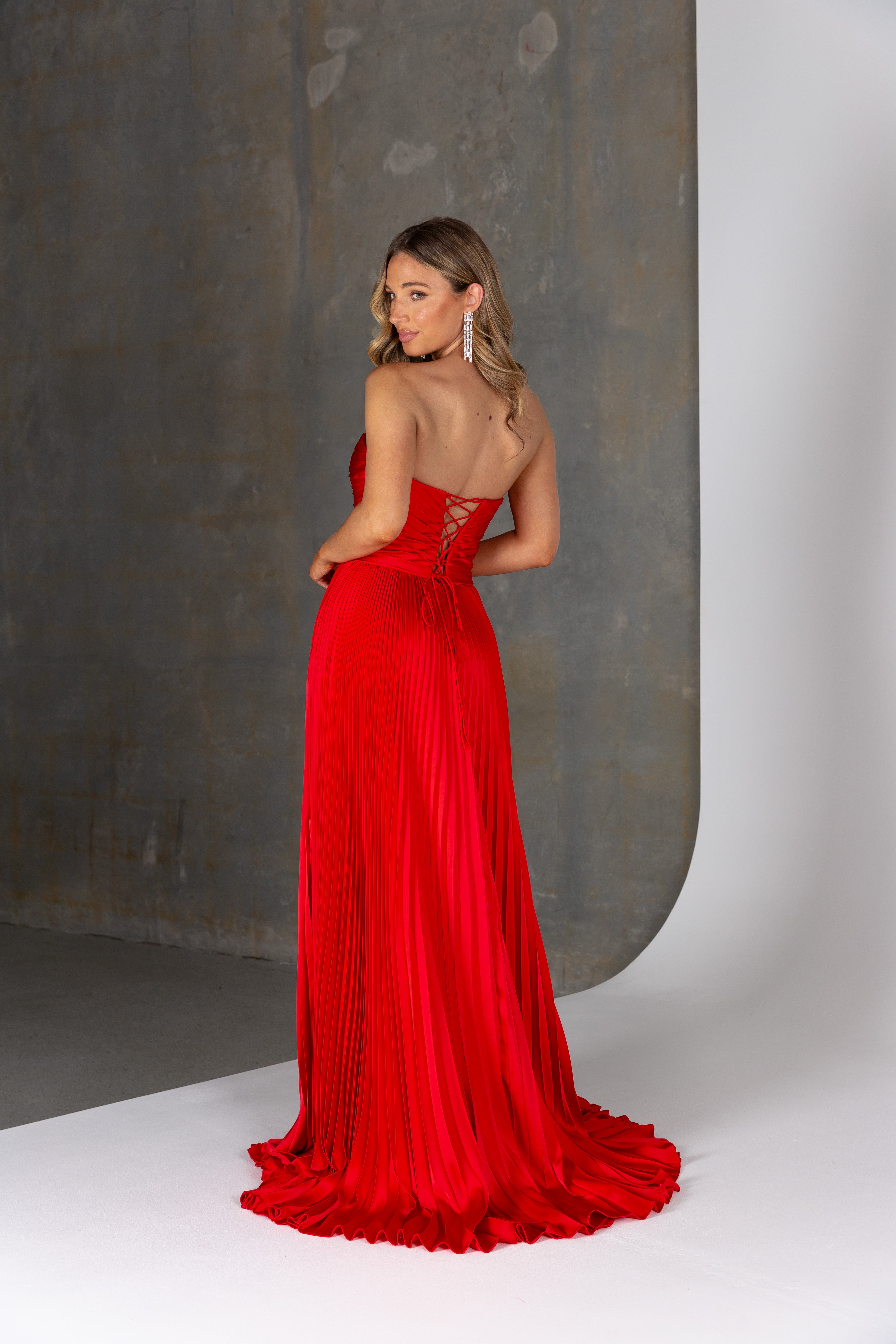 Hera Formal Dress by Tania Olsen – strapless pleated satin gown with corset bodice, lace-up back, leg split & pockets. A-line silhouette made to shine.