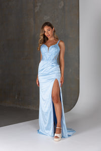 Woman wearing a light blue evening gown with a high slit on a neutral background