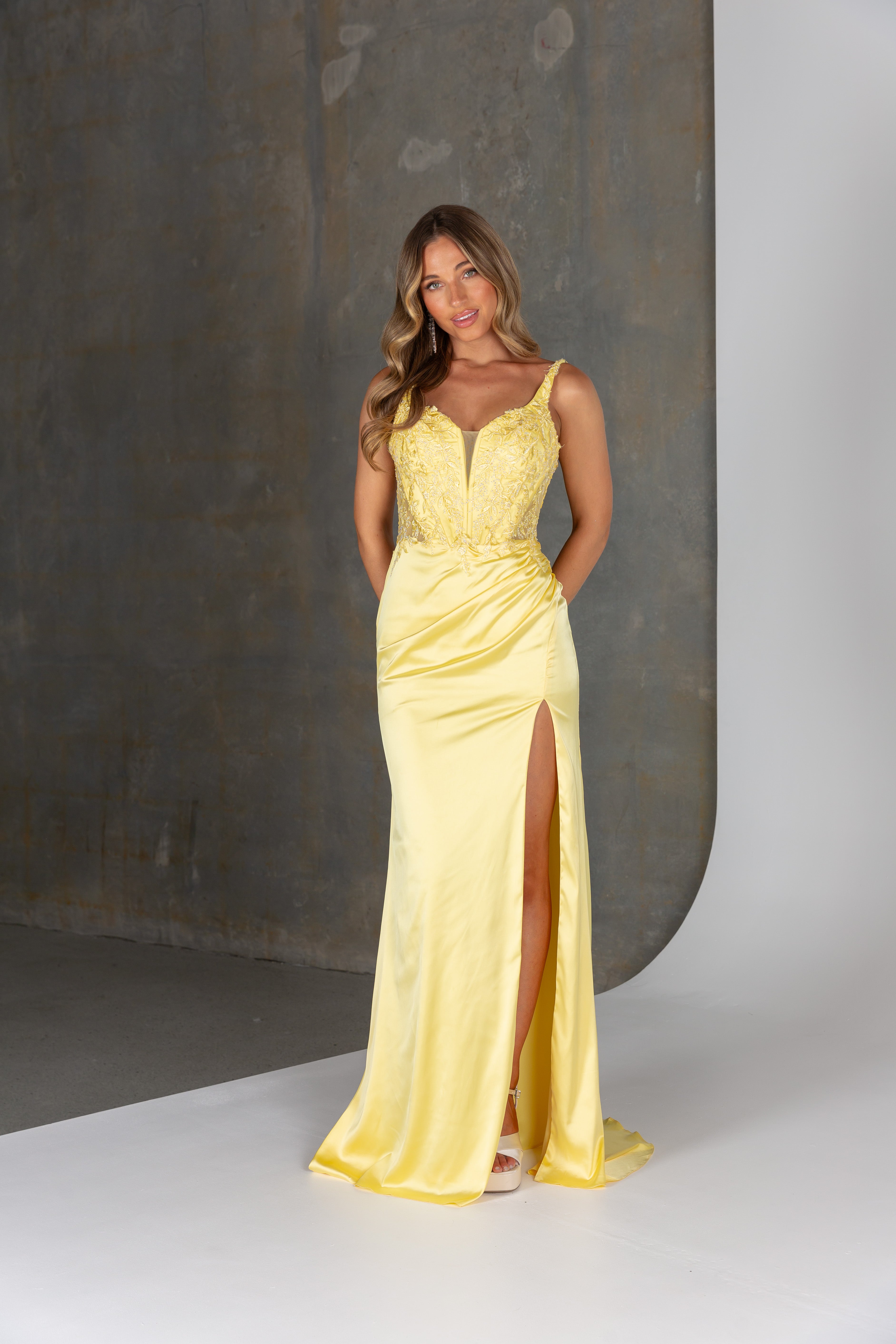 Woman wearing a yellow evening gown with a high slit on a neutral background
