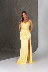 Woman wearing a yellow evening gown with a high slit on a neutral background